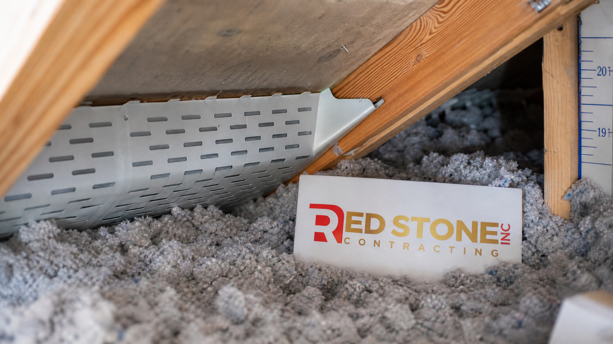 Close-up of properly installed attic insulation baffles and blown-in cellulose material with a small branded sign placard nearby
